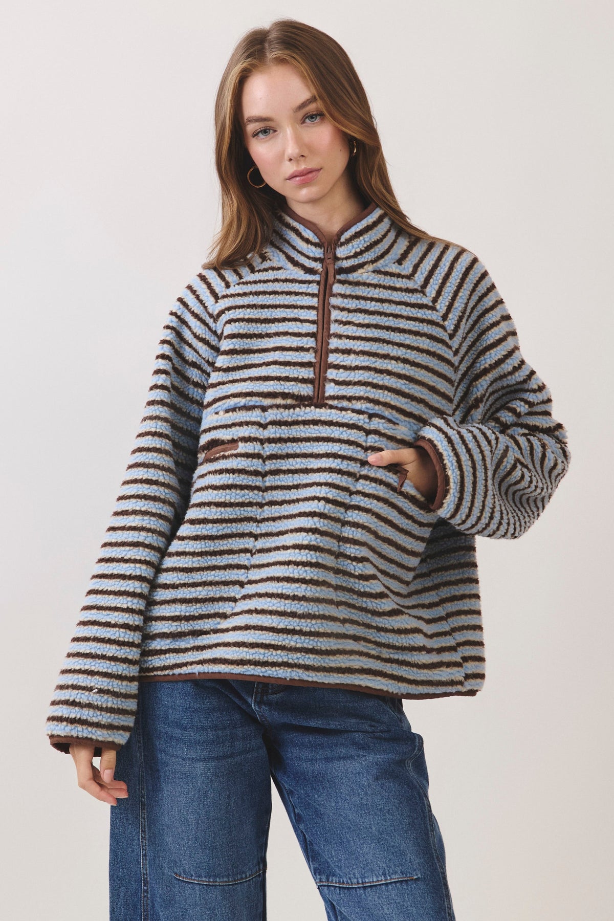 Woman standing on white background wearing a blue and brown striped fleece pullover