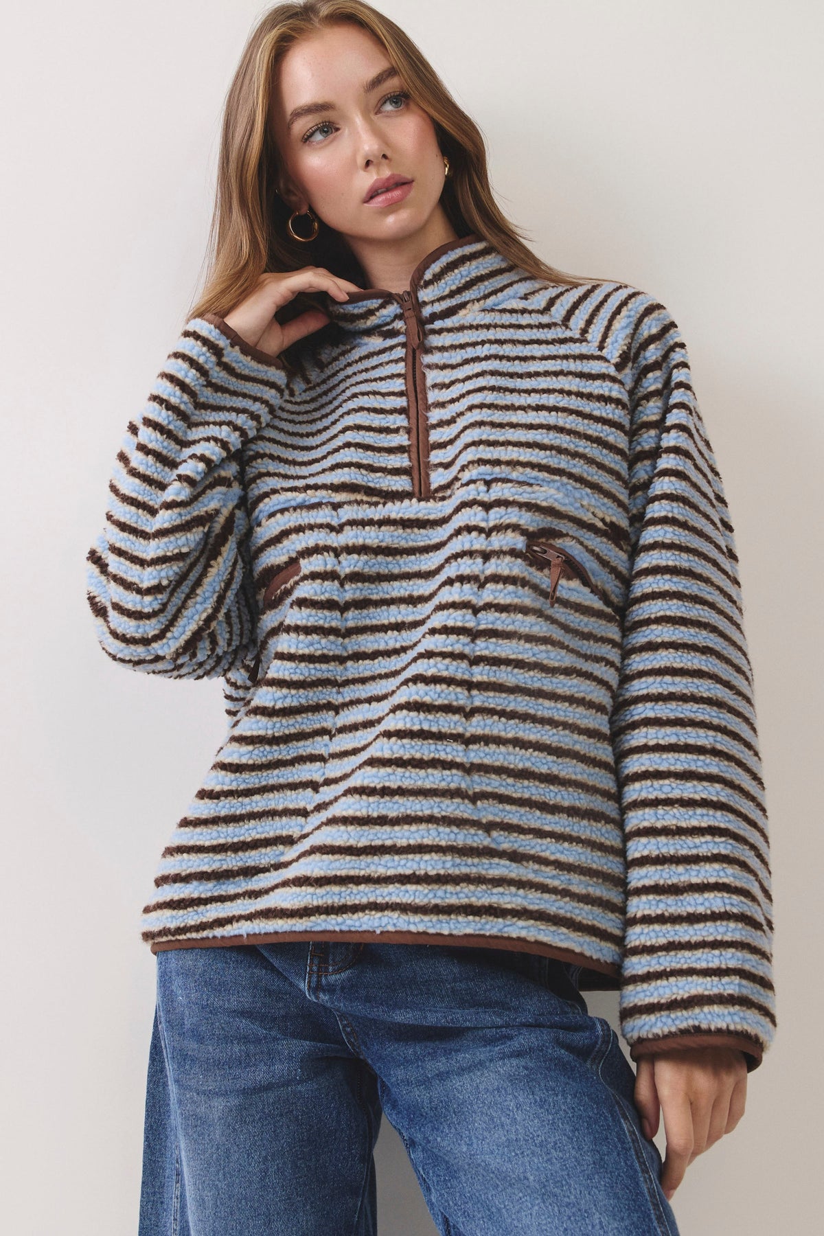 Woman standing on white background wearing a blue and brown striped fleece pullover