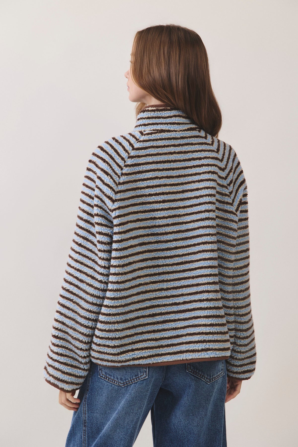 Woman standing on white background wearing a blue and brown striped fleece pullover