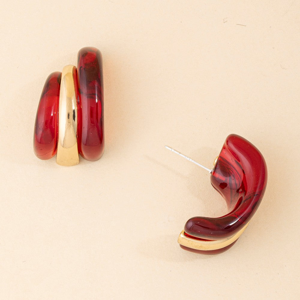 A pair of chunky, curved resin earrings in a deep red and gold marbled pattern, displayed on a light beige background.
