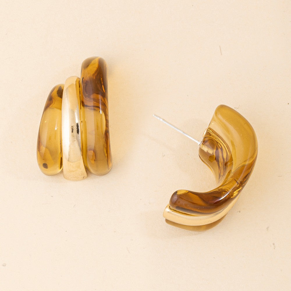 A pair of retro-style crescent-shaped earrings made of marbled amber and brown resin with gold-toned metal edges and posts, displayed on a light beige background.