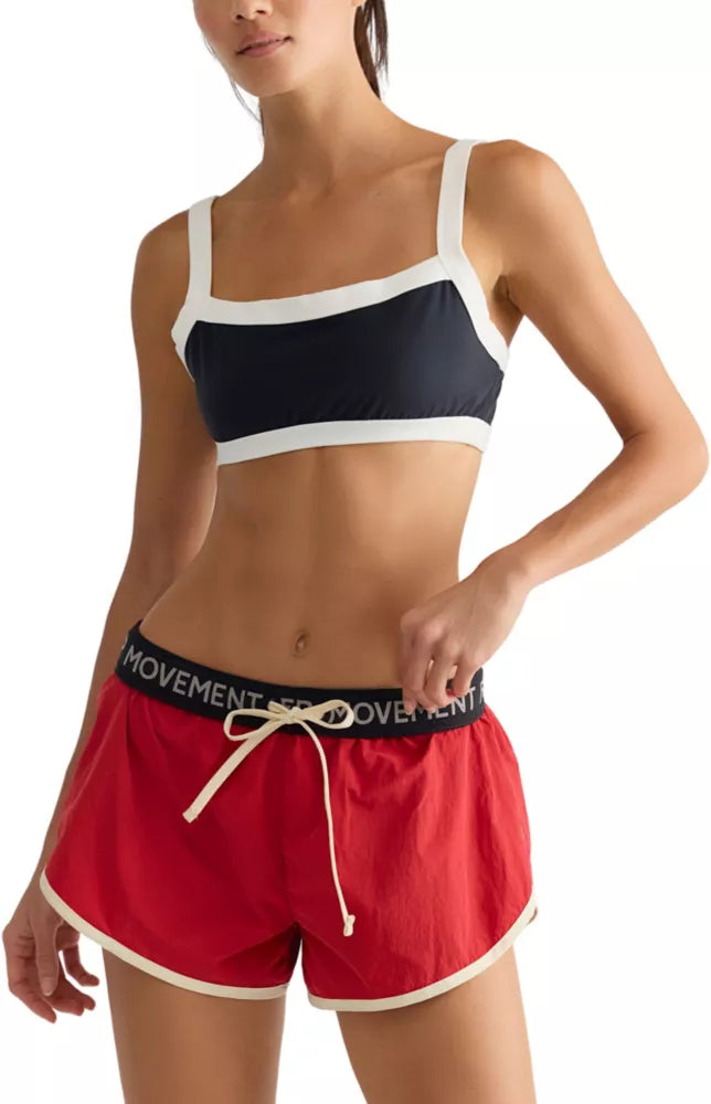 A woman wearing a black  top and red-colored athletic shorts with a black waistband that reads 'FP MOVEMENT'.