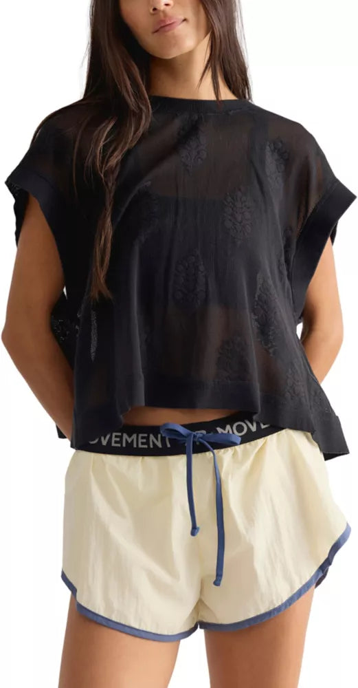 A woman wearing a black sleeveless top and cream-colored athletic shorts with a black waistband that reads 'FP MOVEMENT'.