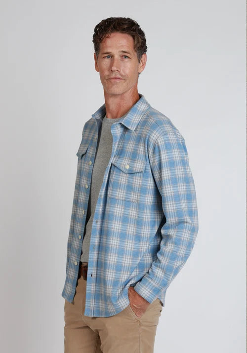 Man standing wearing blue and white button down, khakis, and a belt in front of  a white background