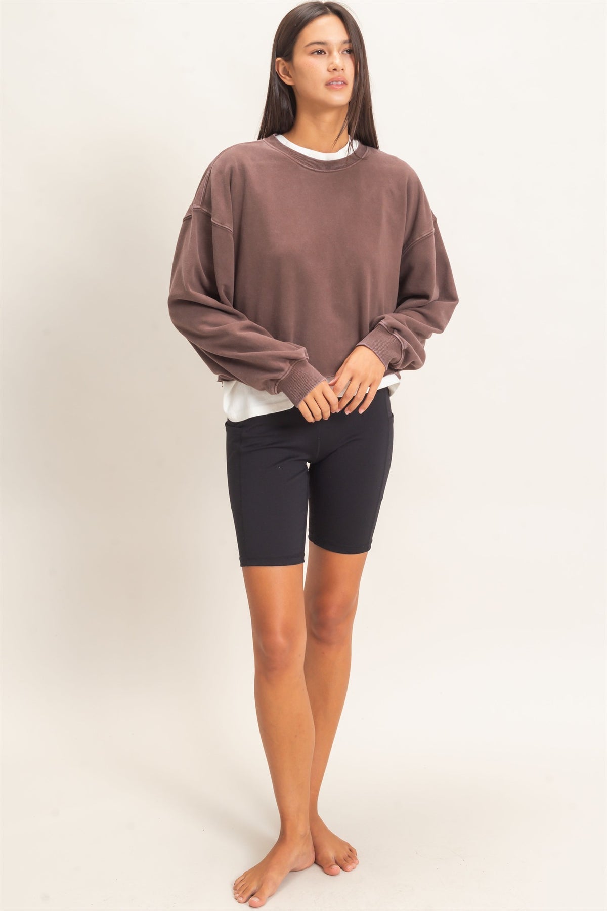 Woman wearing a brown oversized sweatshirt and black shorts on a white background