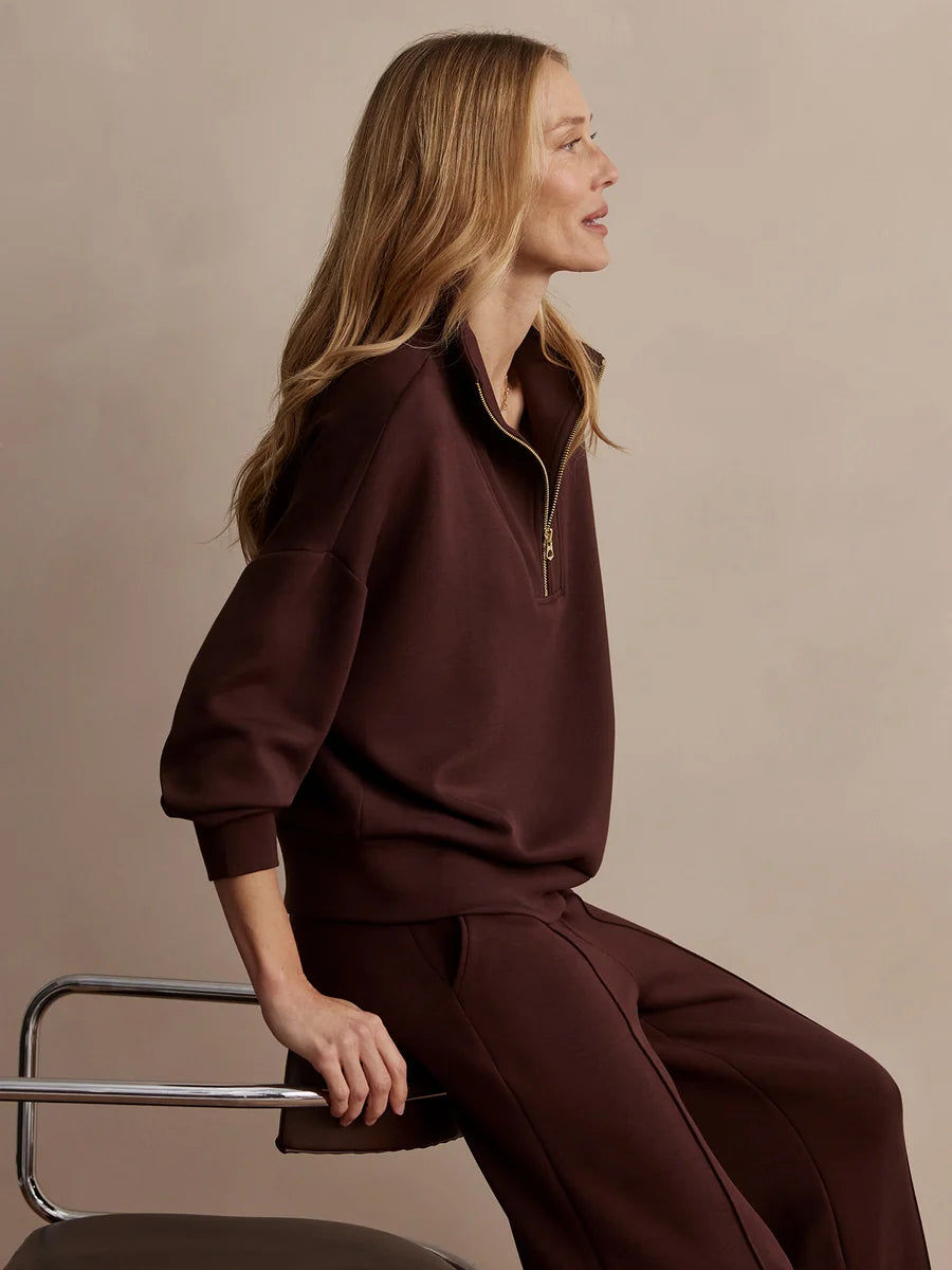 Woman wearing a brown outfit sitting on a chair against a beige background