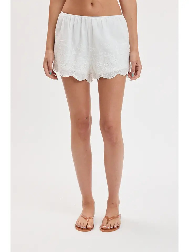 woman standing on white background wearing white eyelet shorts and flip flops