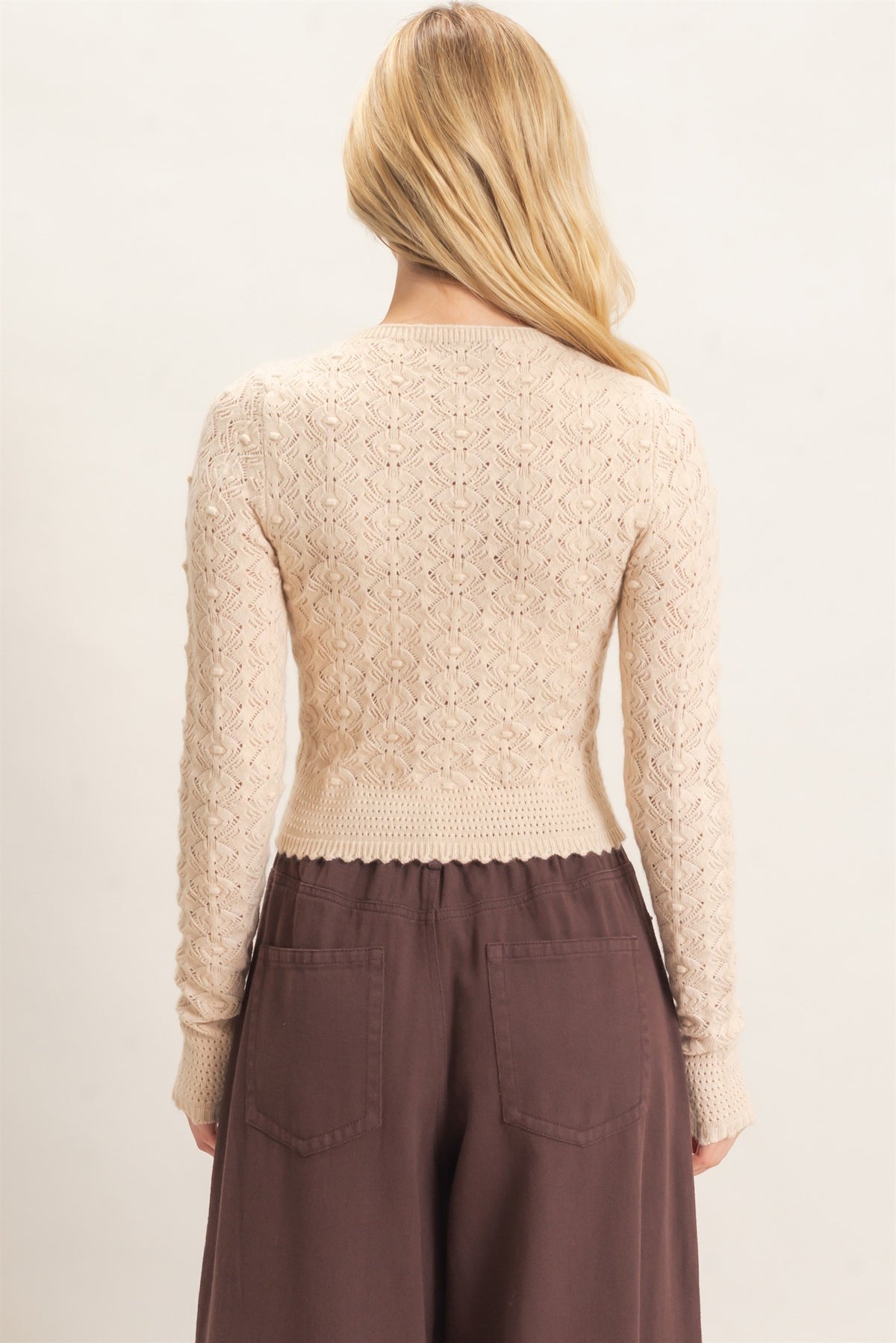 A woman shown from the back wearing a cream-colored textured knit long-sleeve top and dark brown wide-leg pants against a plain light background.