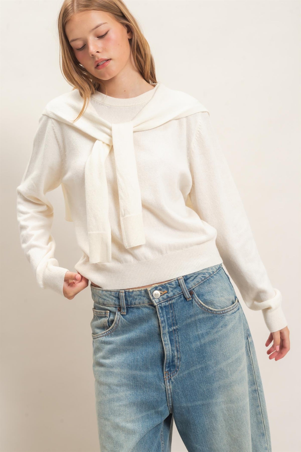 woman standing on white backdrop wearing cream sweater and jeans 