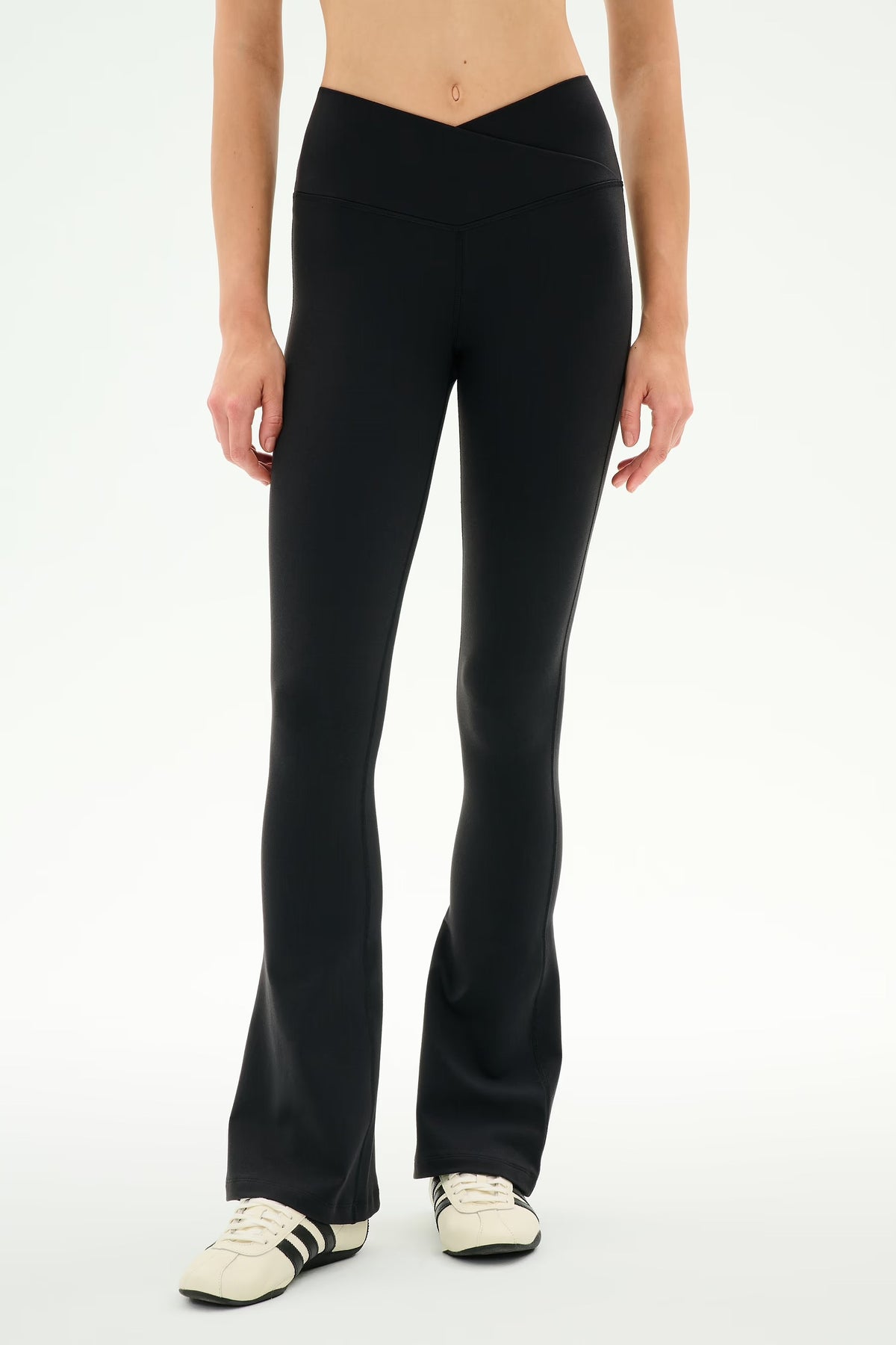 A model wearing black flared leggings or pants with white sneakers, shown from the waist down against a plain white studio background.