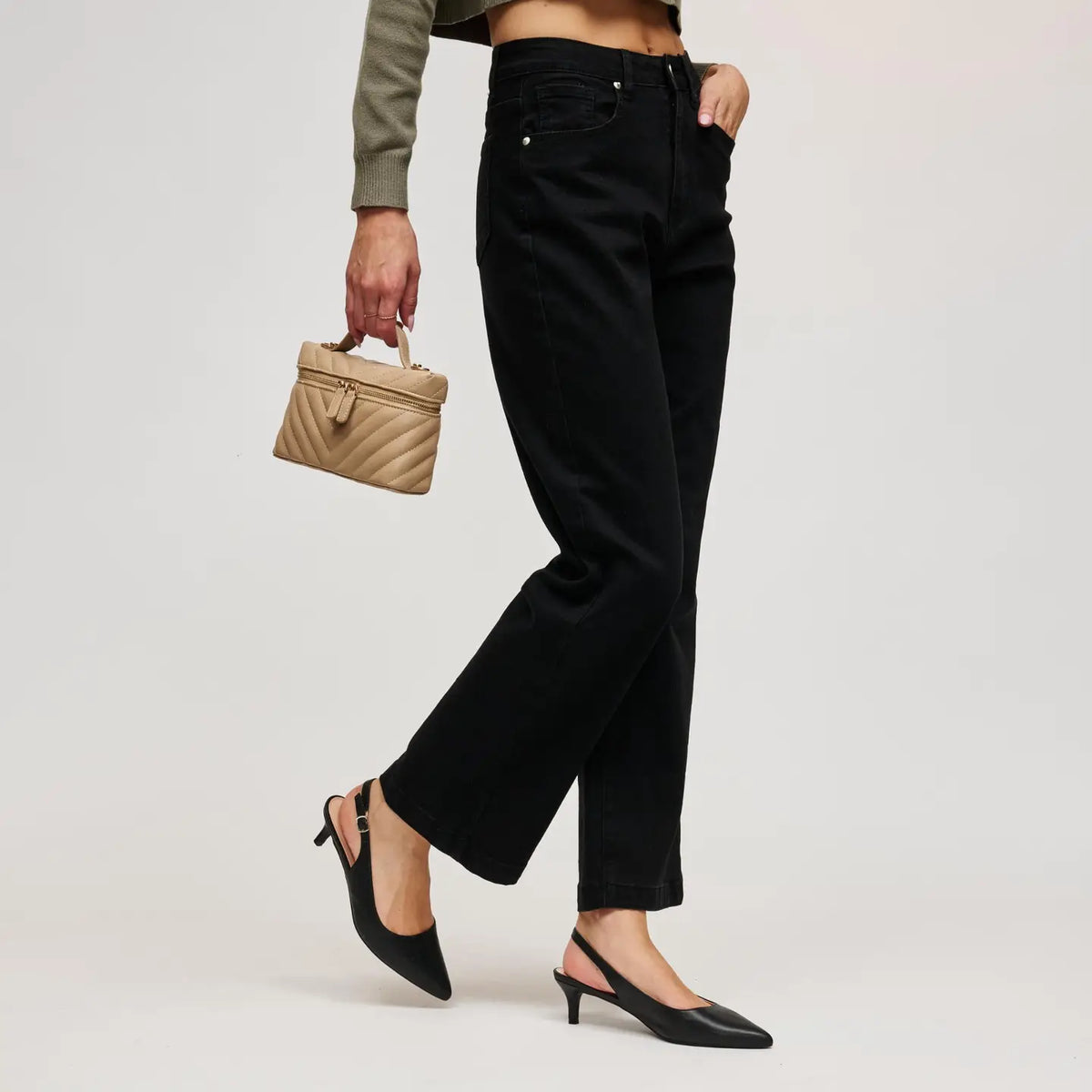 A model wearing black wide-leg cropped jeans, black slingback kitten heels, and holding a small beige quilted handbag against a light gray studio background.