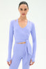 A woman modeling a light periwinkle blue long-sleeve wrap top and matching leggings against a plain white studio background.