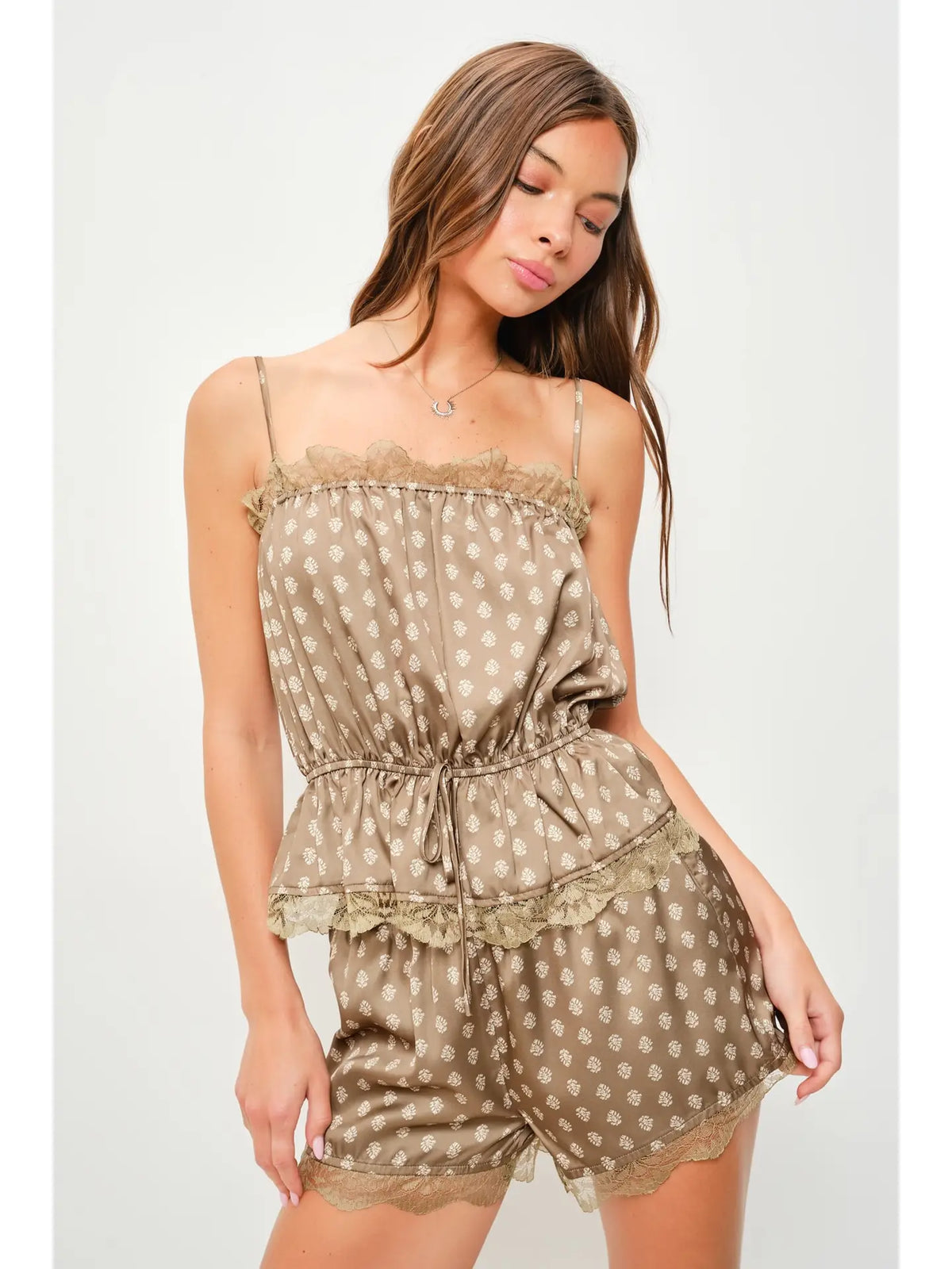 A woman modeling a two-piece satin pajama set featuring a brown and beige polka dot pattern with lace trim, consisting of a camisole top and matching shorts.