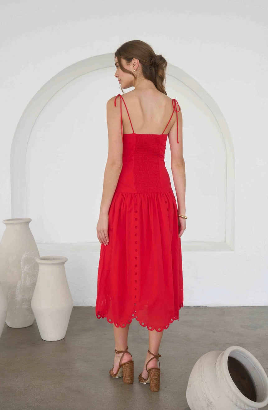 Woman wearing a red dress standing in a minimalistic room with white arch and vases.