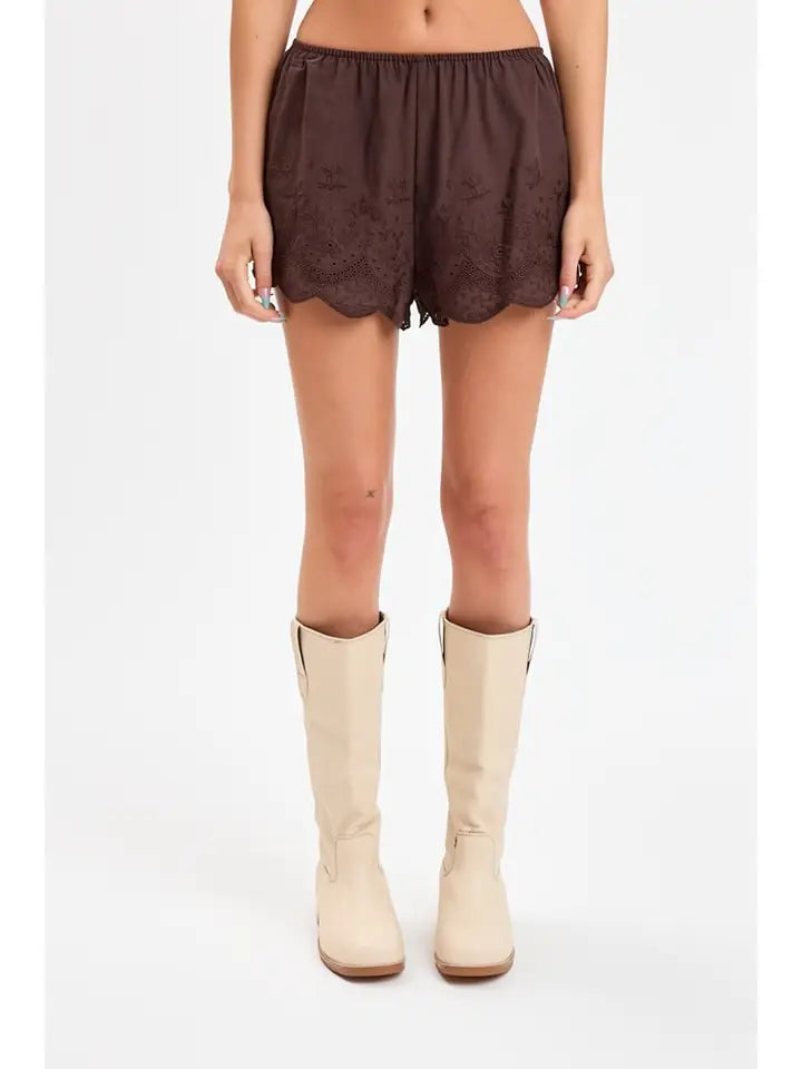 woman standing on white background wearing brown eyelet shorts and boots