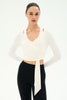 A woman modeling a white long-sleeve wrap-style crop top with a front tie detail, paired with black leggings, against a plain white studio background.