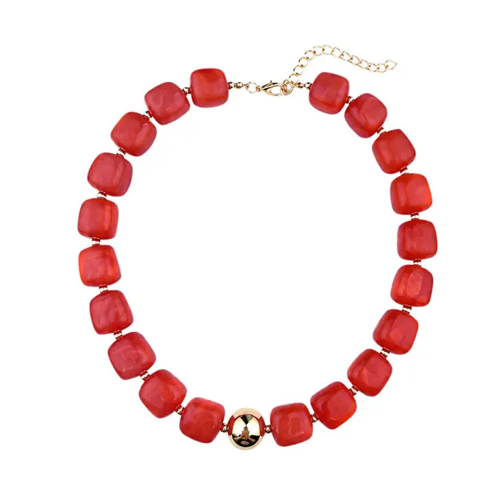 A red beaded necklace with chunky, rounded square beads and a central gold-toned metallic accent, displayed on a clean white background.