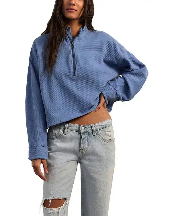Person wearing a blue cropped sweater and light gray jeans on a white background