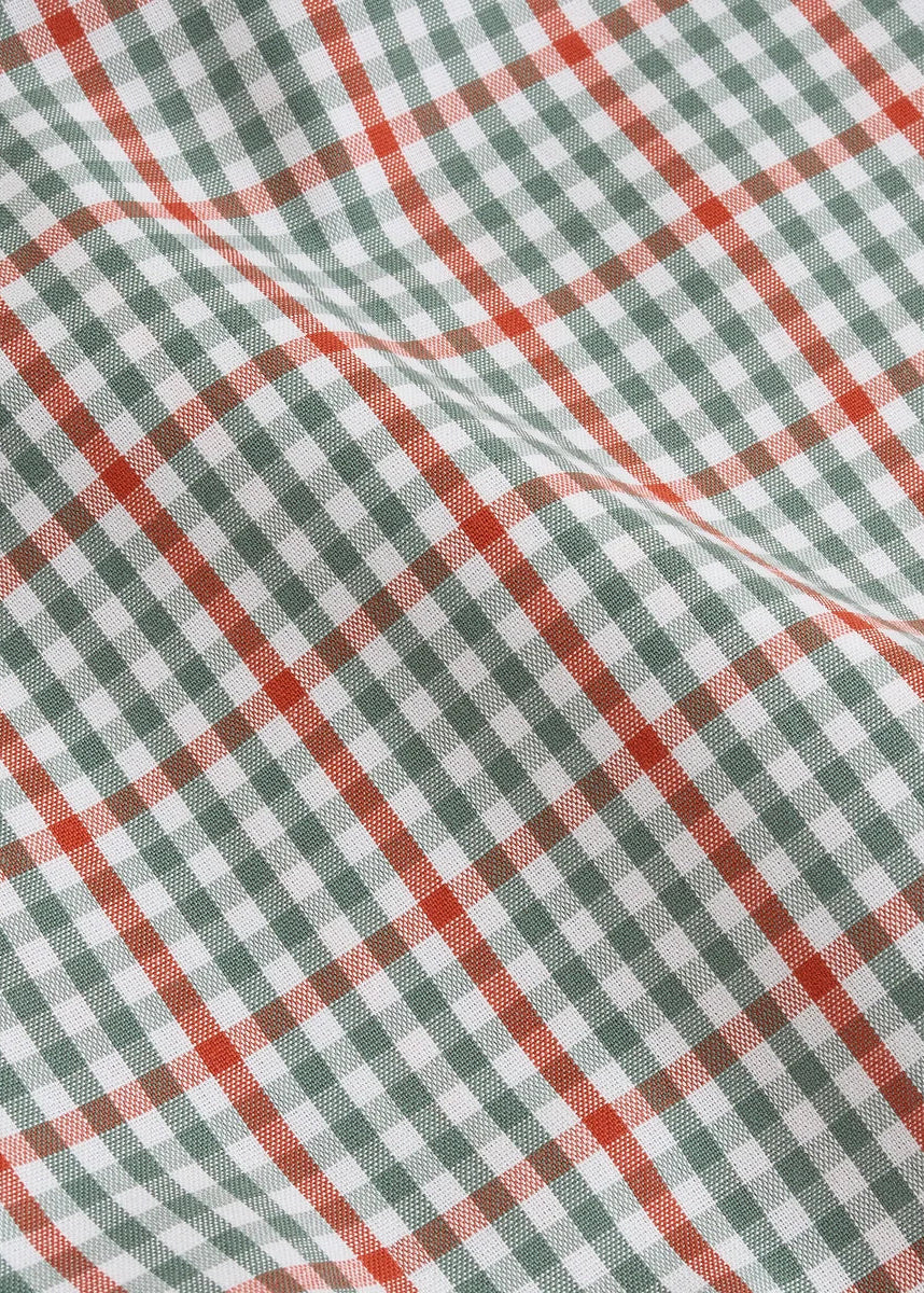 A close-up of a white fabric with a green and red gingham plaid pattern, showing its woven texture and soft folds.
