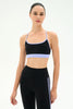 A woman modeling a black sports bra with light purple trim and matching high-waisted black leggings with white side stripes, against a plain white studio background.