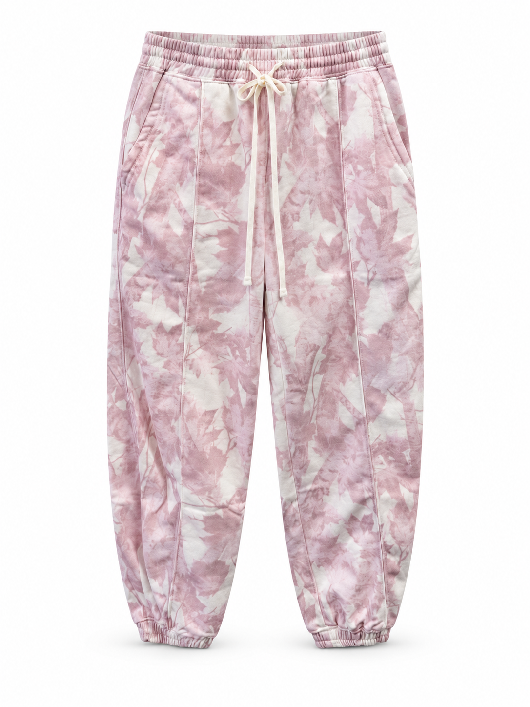 Ivory joggers with a muted pink and mauve woodland camouflage print, cream drawstring waistband, side pockets, front seams, and elastic ankle cuffs on a white background.