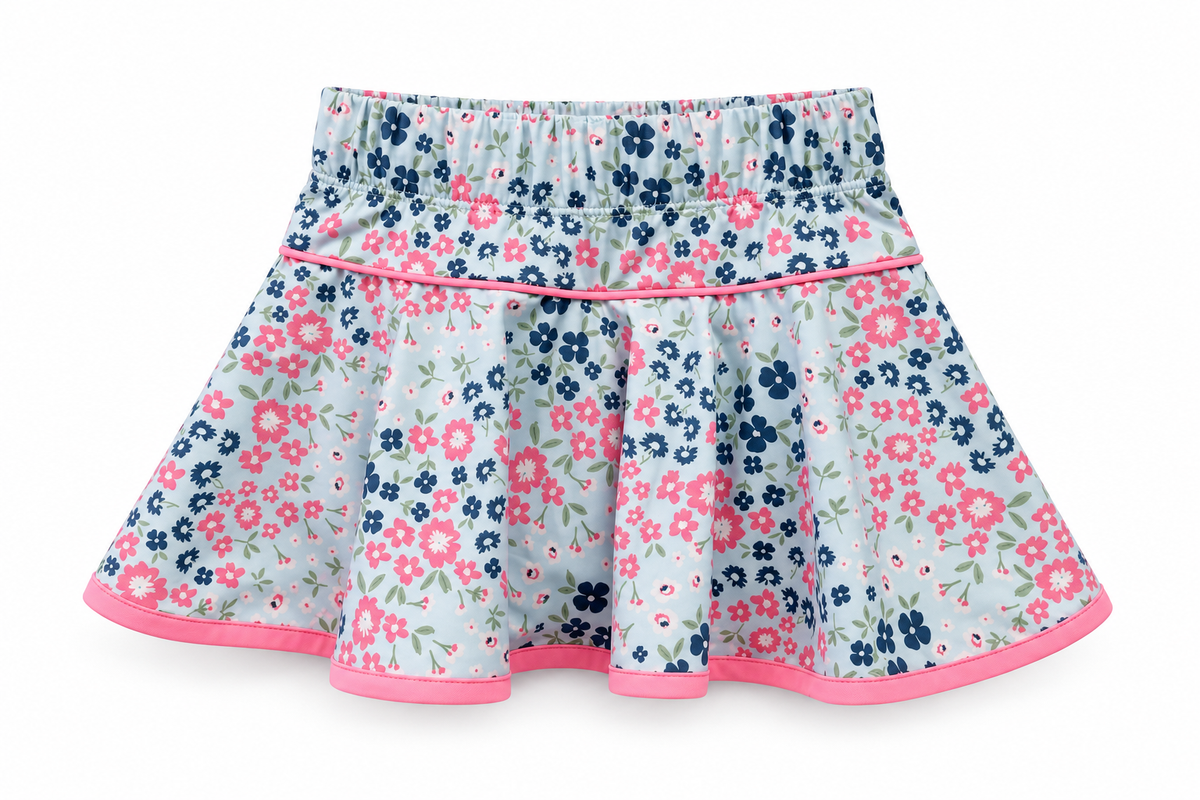 A girls' flared skirt with a light blue-gray background, covered in a pink and navy floral print, finished with a pink elastic waistband and pink trim along the hem.