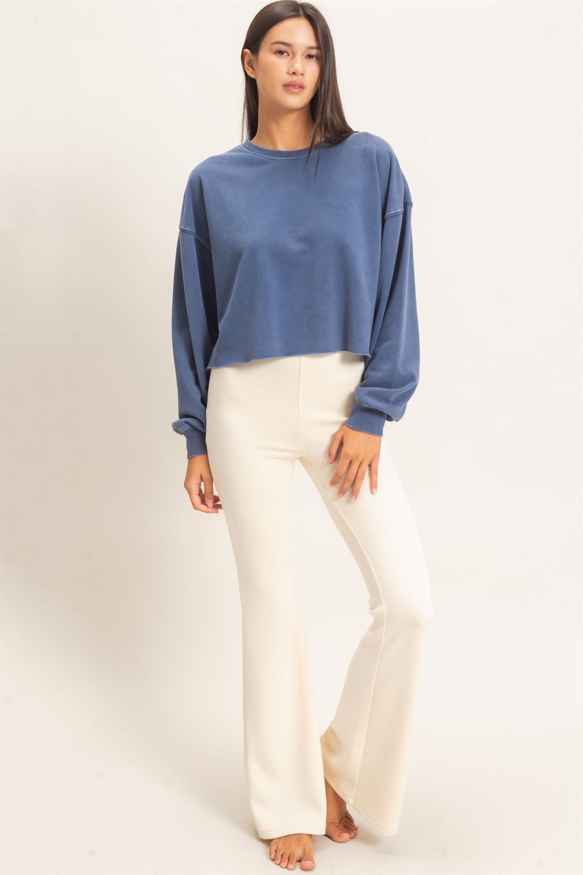 Woman wearing a blue sweater and white pants on a plain background