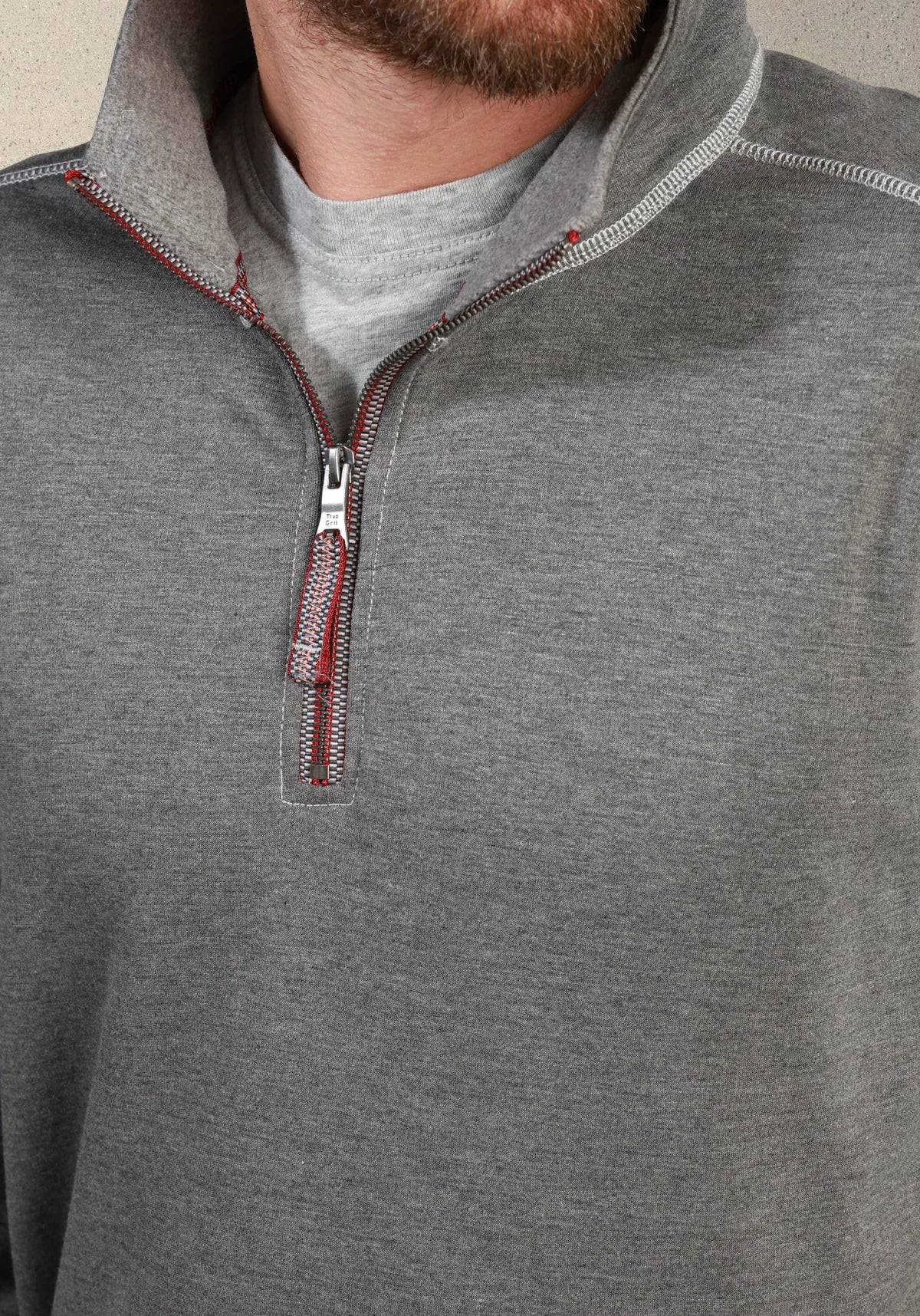 Close-up of a man wearing a heather gray quarter-zip pullover with a silver zipper and red stitching accents, layered over a light gray t-shirt.