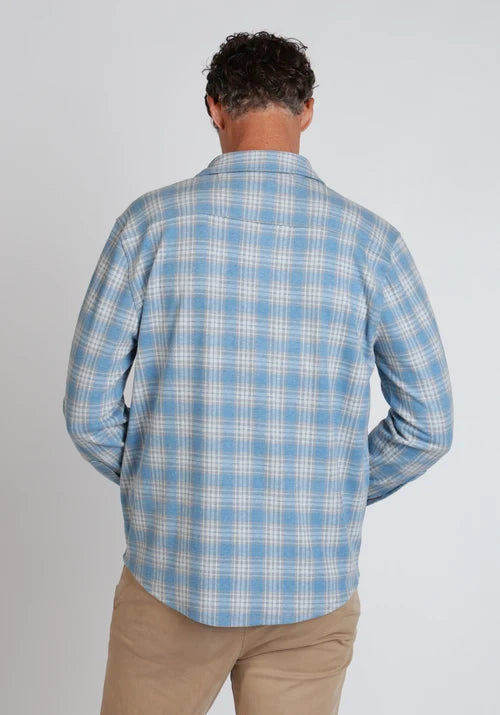 Man standing wearing blue and white button down, khakis, and a belt in front of  a white background