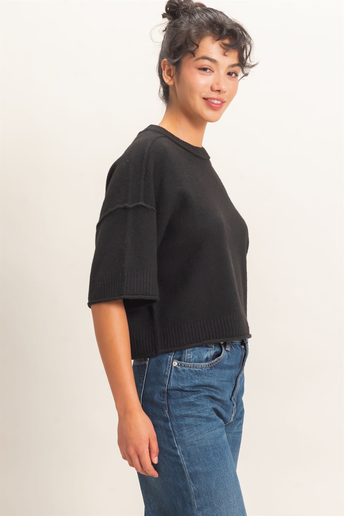 Woman wearing a black sweater and blue jeans on a plain background