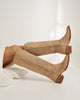 Pair of beige knee-high boots with brown soles on a white background