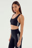 Woman wearing a black sports bra and leggings with white stripes on a light gray background
