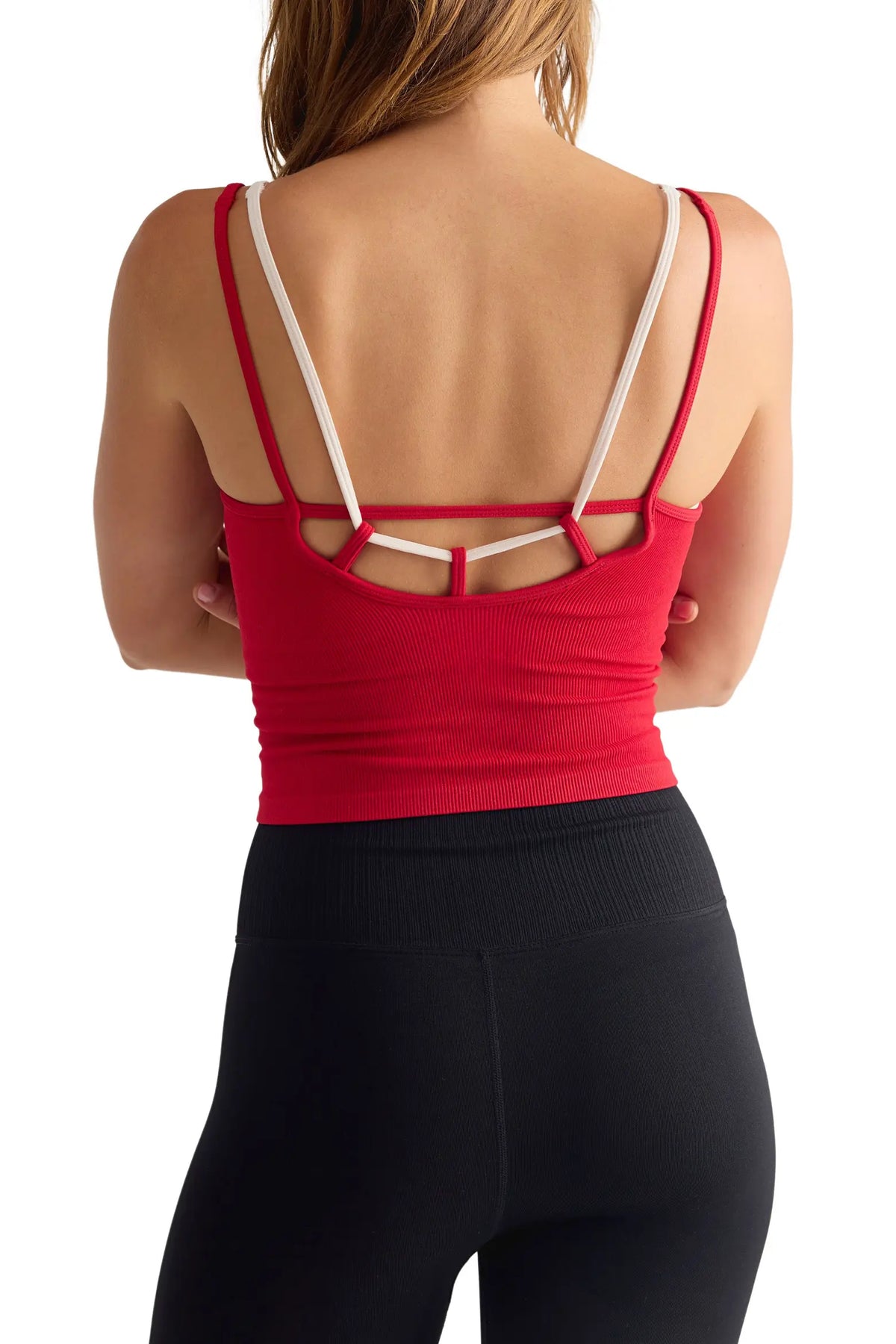 A woman shown from the back wearing a red sports bra with white crossover straps and black leggings against a plain white background.