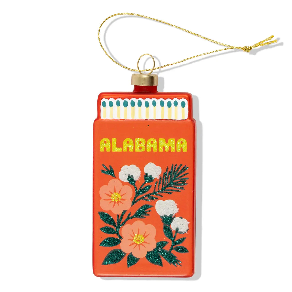A decorative Christmas ornament shaped like a matchbox with the word 'ALABAMA' in yellow glitter lettering and a floral design below. The ornament is orange-red with pink flowers, green leaves, and white blossoms, hanging from a gold string on a white background.
