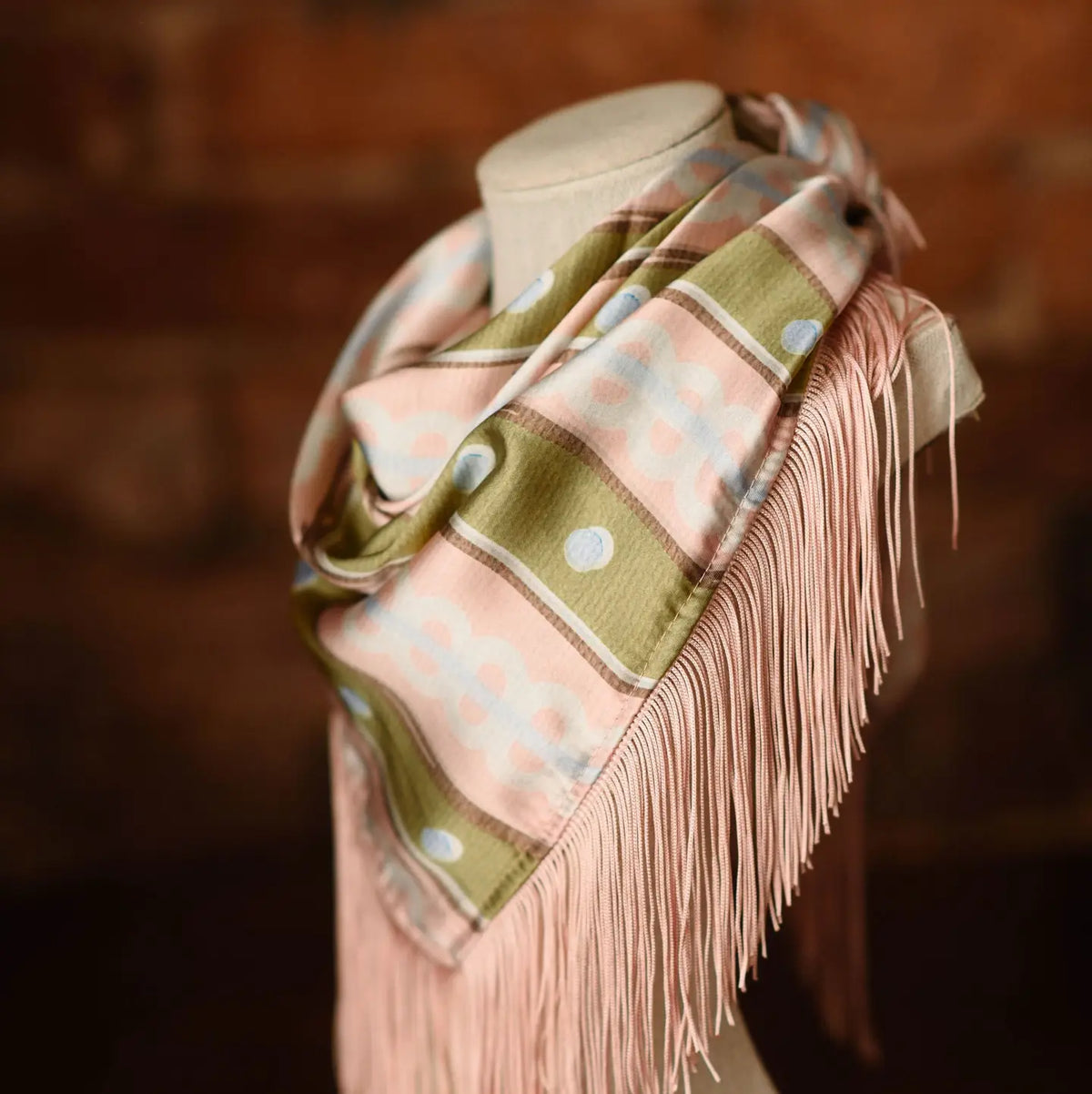 Patterned square scarf in blush pink and olive green featuring long pink fringe trim.