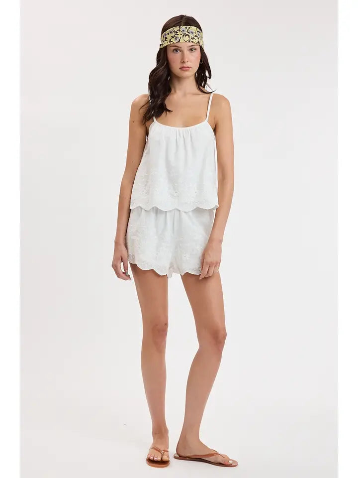 woman standing on white background wearing a white tank top and white shorts