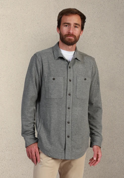 Man wearing a gray button down and khakis in front of tan background