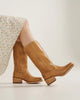 Tan leather boots worn with a floral skirt on a light background