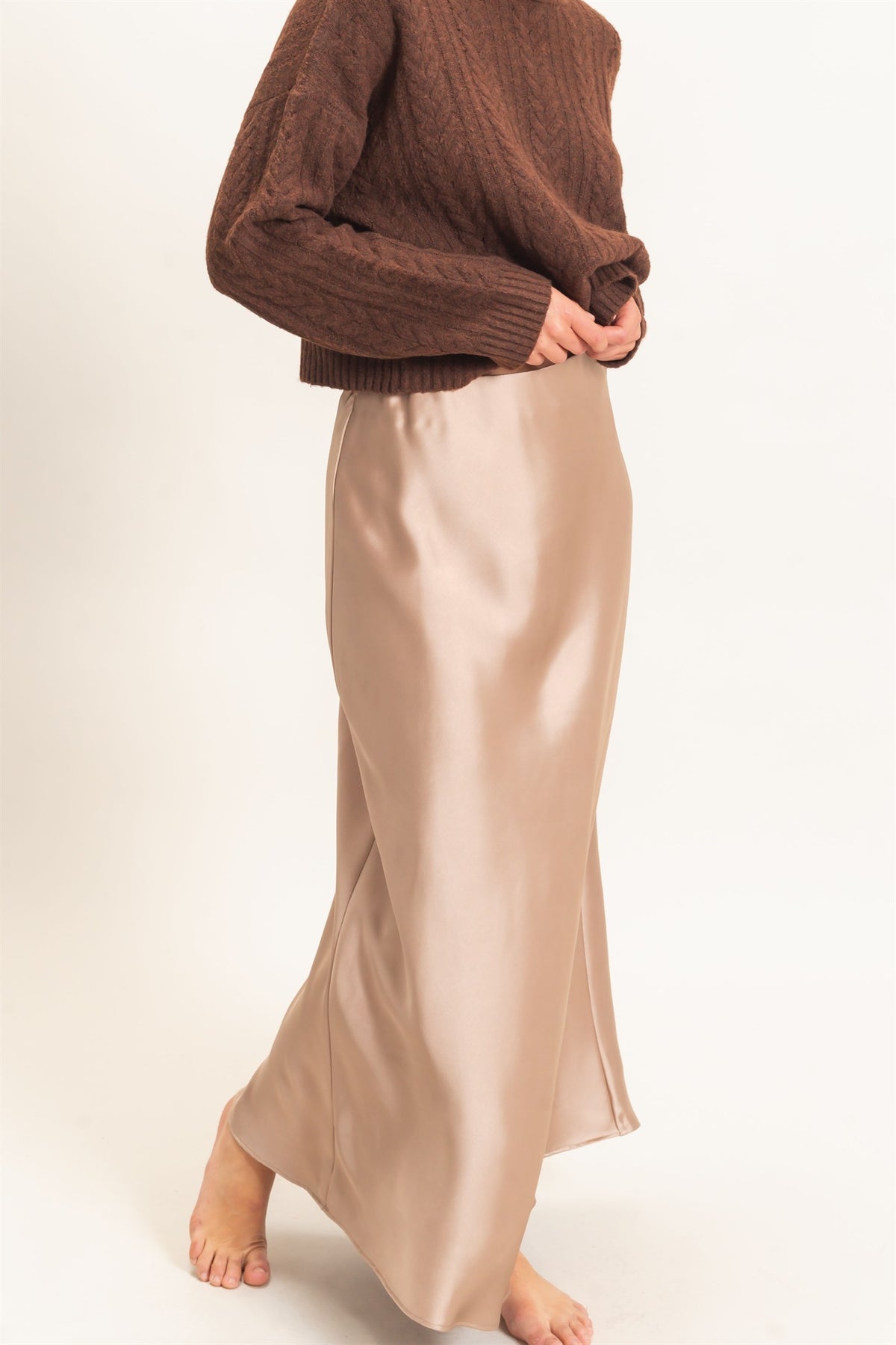 Person wearing a brown sweater and beige satin skirt on a white background