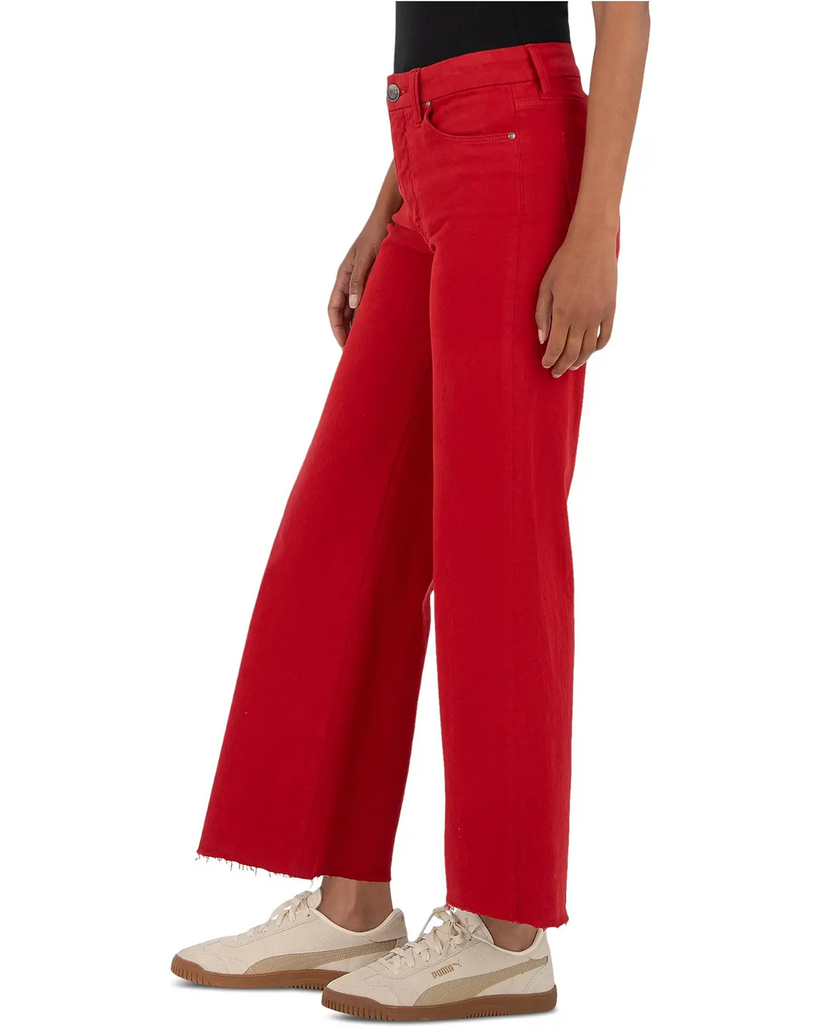 A model wearing bright red wide-leg cropped jeans with a raw frayed hem, paired with cream sneakers, shown from the waist down on a white background.