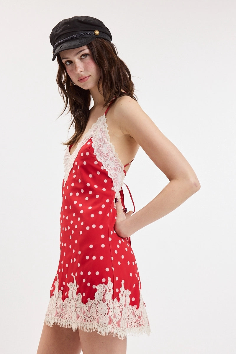 Woman wearing a red polka dot dress with white lace trim and a black cap on a white background