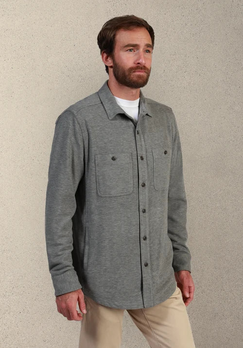 Man wearing a gray button down and khakis in front of tan background