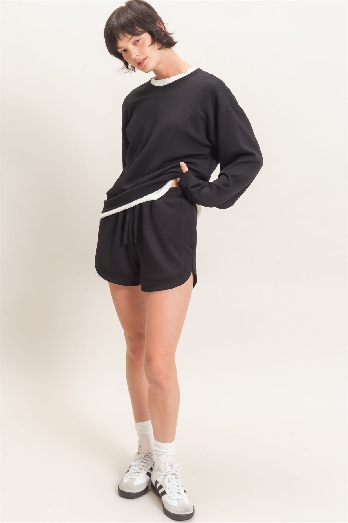 Person wearing a black outfit with white sneakers on a plain background