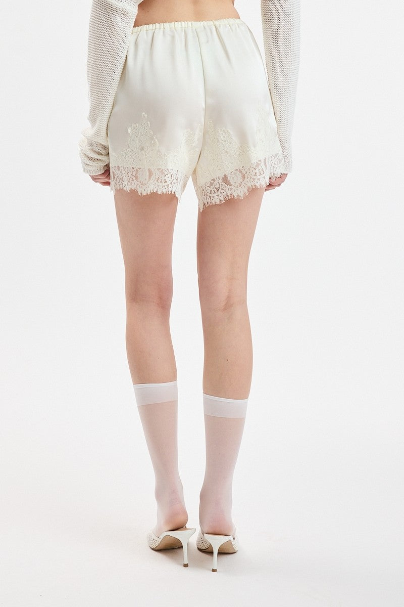 Person wearing white lace shorts on a plain background