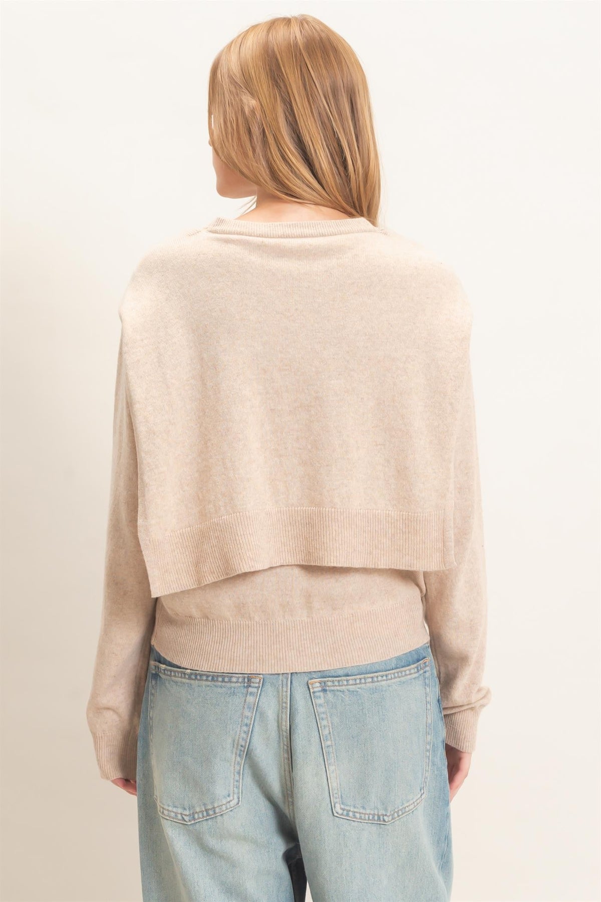 woman standing on white backdrop wearing beige sweater and jeans 
