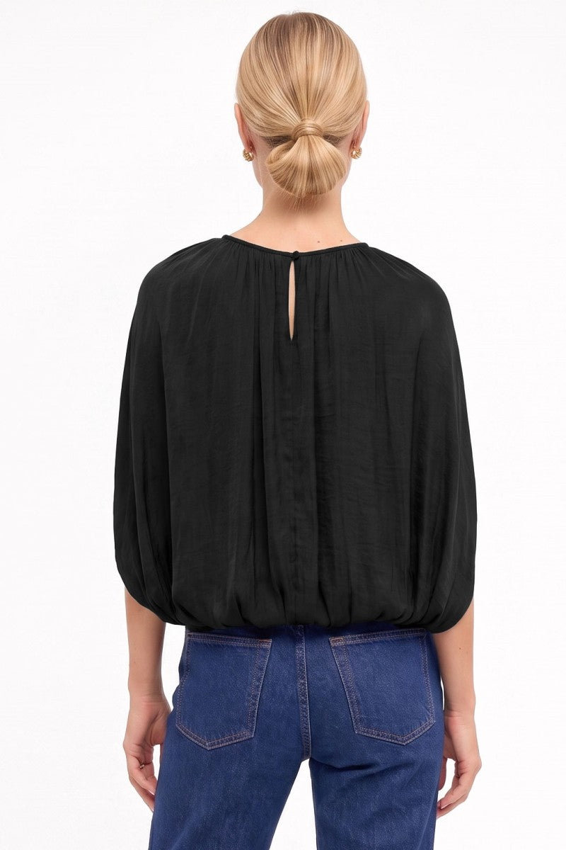 A woman viewed from the back wearing a black long-sleeve blouse with a small center back slit and blue jeans, against a plain white studio background.