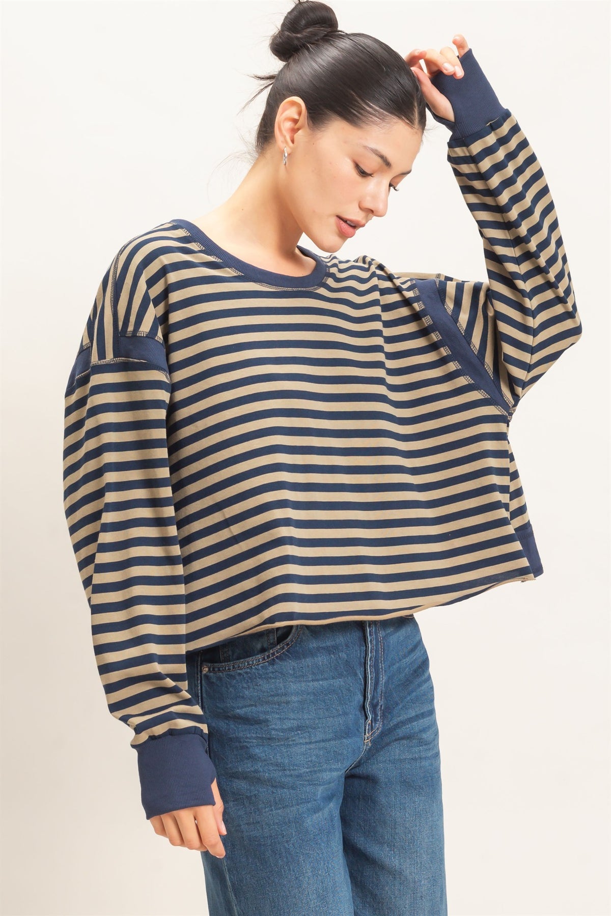 A woman modeling a navy and tan striped shirt while touching her head slightly 