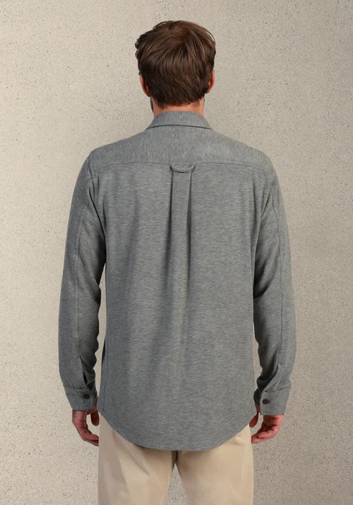 Man wearing a gray button down and khakis in front of tan background