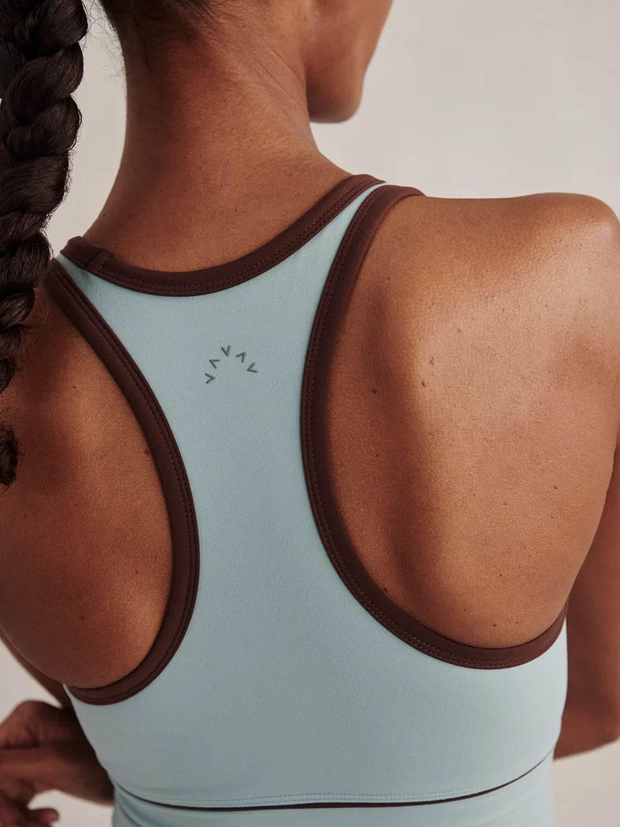 Close-up back view of a woman wearing a light blue athletic sports bra with dark brown trim and a small visible Y-ALOO logo on the upper back.