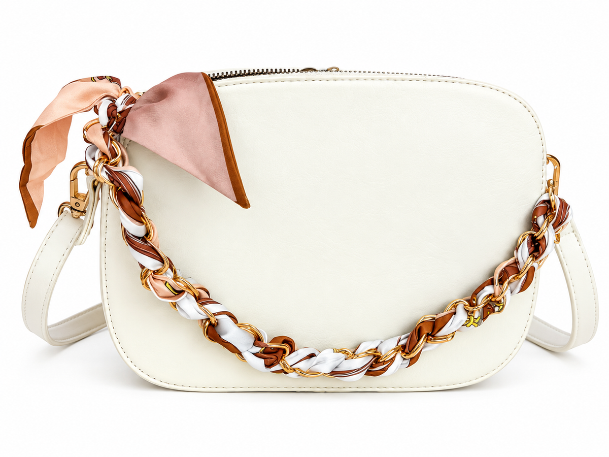 An off-white leather shoulder bag featuring a decorative chain strap woven with white, brown, and gold, accented by a blush pink silk scarf tied in a bow on the side.